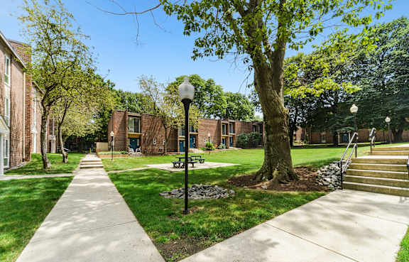 A tree-lined walkway leads to a brick building.