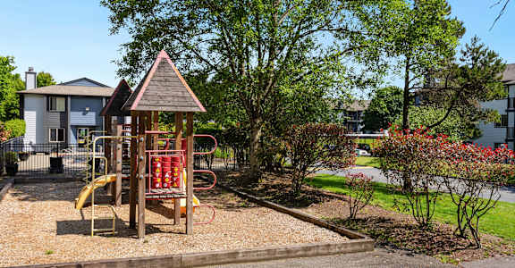 a playground in a park with a house in the background at Eagles Landing Apartments, Everett Washington