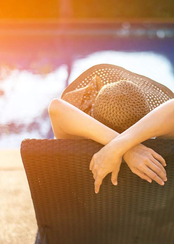 Woman in Sun Hat Laying in Lounge Chair by Swimming Pool
