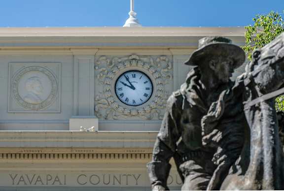 A statue of a man in a hat stands in front of a building with a clock on it.