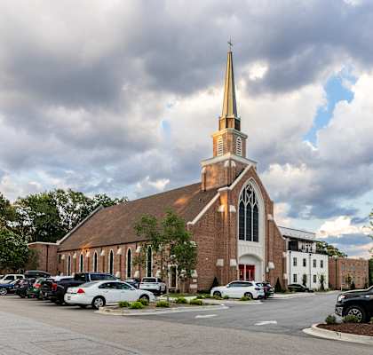 a church with a steeple and a building with cars parked in front
