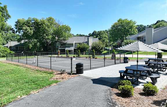A sunny day at a park with picnic tables and a tennis court.
