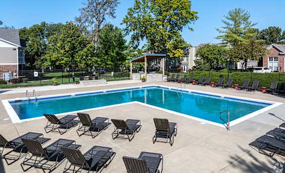 A pool surrounded by lounge chairs and trees.