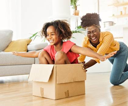 a mother and daughter sitting on the floor with a cardboard box