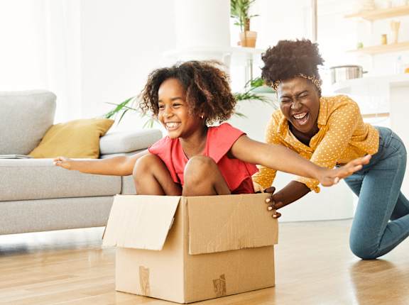 a mother and daughter sitting on the floor with a cardboard box