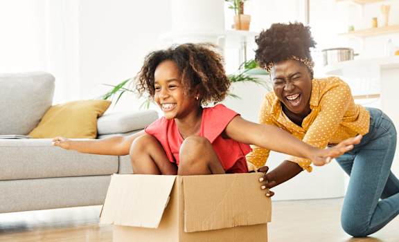 a mother and daughter sitting on the floor with a cardboard box