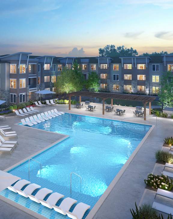 A large swimming pool surrounded by lounge chairs and umbrellas in front of apartment buildings.