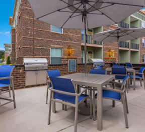 a patio with a grill and tables with blue chairs and umbrellas