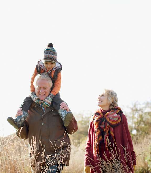 a young child sitting on the shoulders of a man and woman as they walk through a field