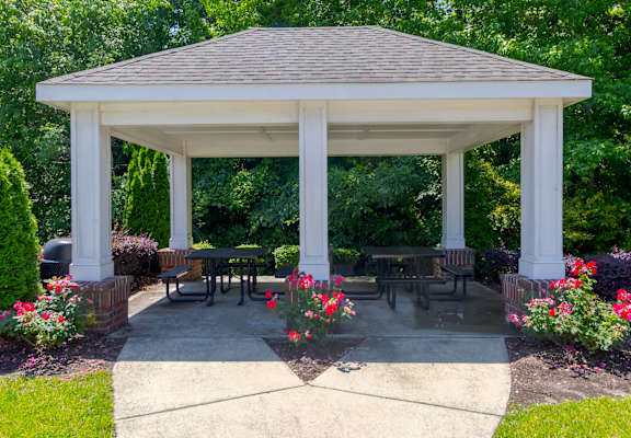 A white gazebo with a brown roof is surrounded by flowers and greenery.