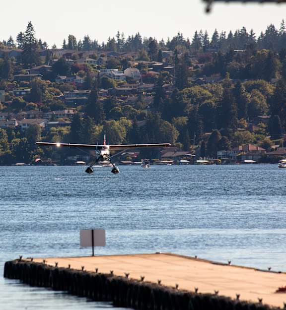 A helicopter flies over a body of water with a pier and a sign in the foreground.
