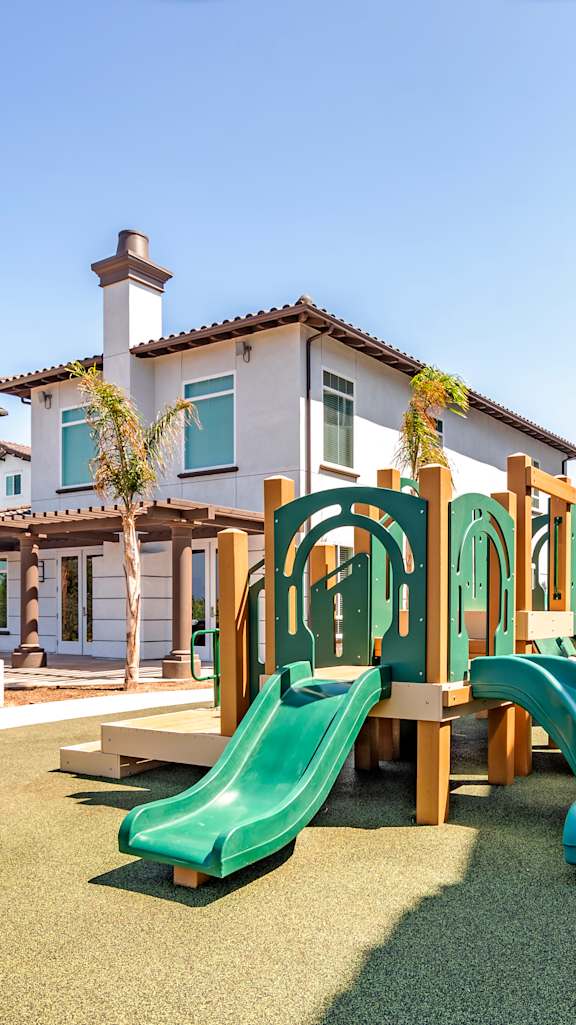 A playground with a green slide and a wooden structure.