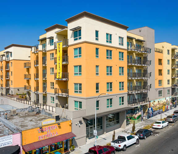 A street view of a yellow and white apartment building with cars parked in front.