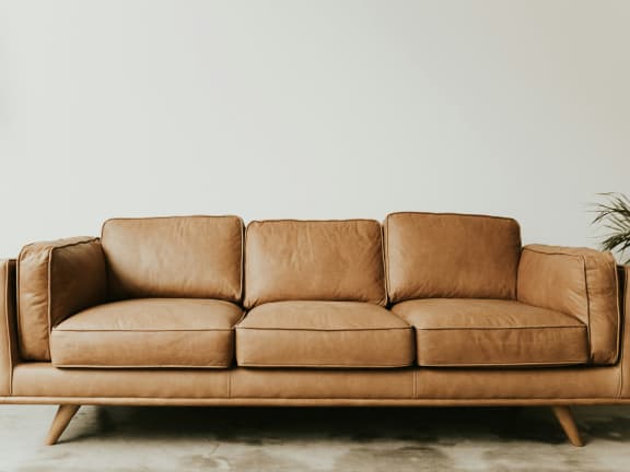 A brown leather couch is placed in a room with a plant beside it. at Greens at Stonecreek, Georgia