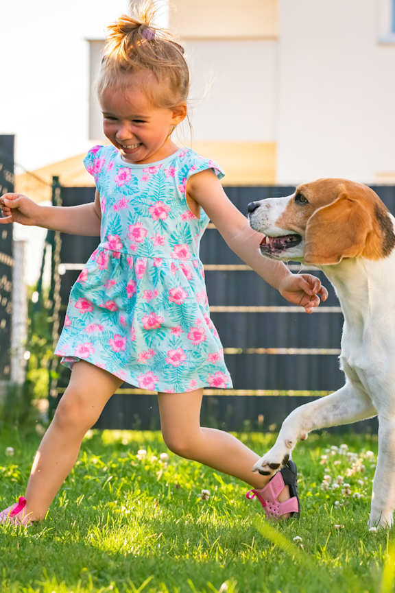 A little girl is playing with a dog in a yard.