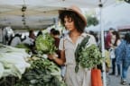 a woman holding a bunch of cabbages at a farmers market