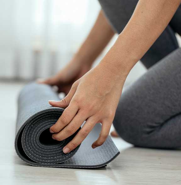 A person is rolling up a grey yoga mat.