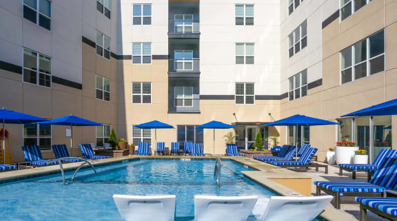 a swimming pool with chairs and umbrellas in front of a building at Aster Apartments, Beachwood Ohio