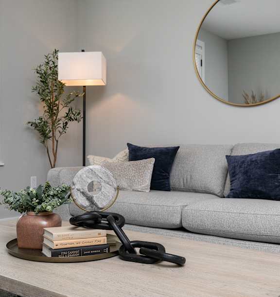 A living room with a grey couch, a wooden coffee table, and a round mirror on the wall. at The Cunningham Apartments, West Des Moines, IA, 50266