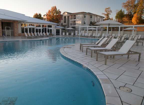 A large outdoor swimming pool with sun loungers and a building in the background.
