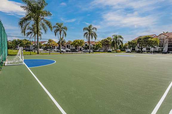 A tennis court surrounded by palm trees and residential buildings.