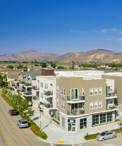 A large apartment complex is situated on a street with cars parked on the side.