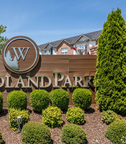 a sign that says woodland park with bushes in front of it