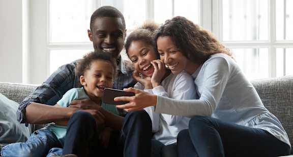 A family of four is sitting on a couch together.