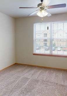 an empty living room with a large window and a ceiling fan