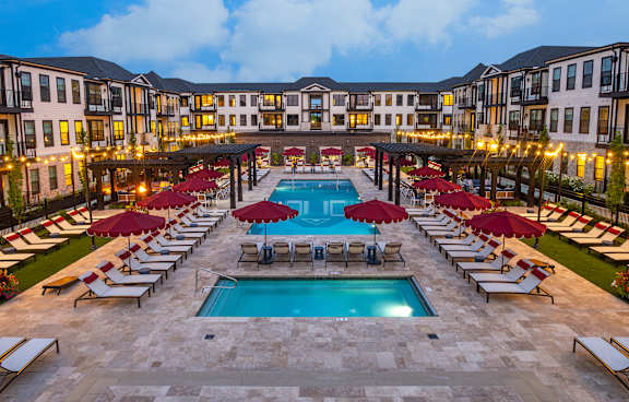 A large pool surrounded by red umbrellas and lounge chairs.