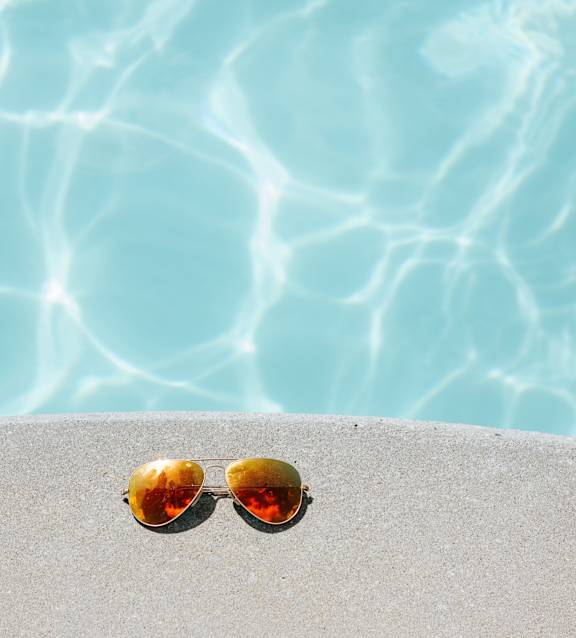 A pair of sunglasses is placed on the edge of a pool.