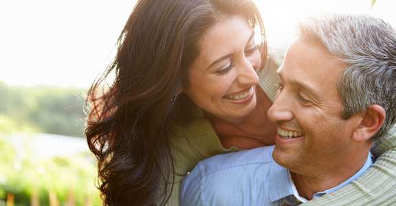 A man and woman are embracing each other in a sunny outdoor setting.