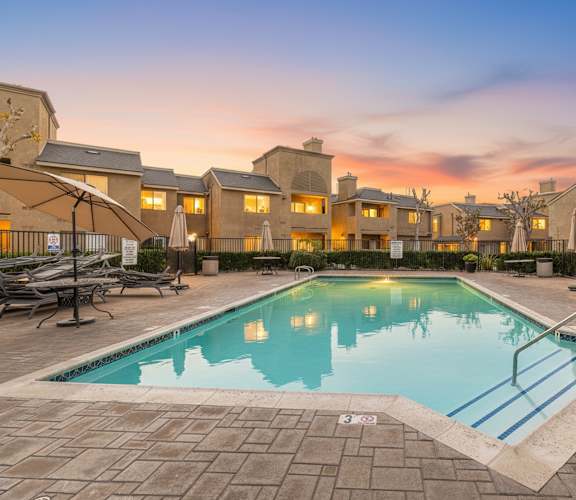 A swimming pool surrounded by a brick patio and lounge chairs.