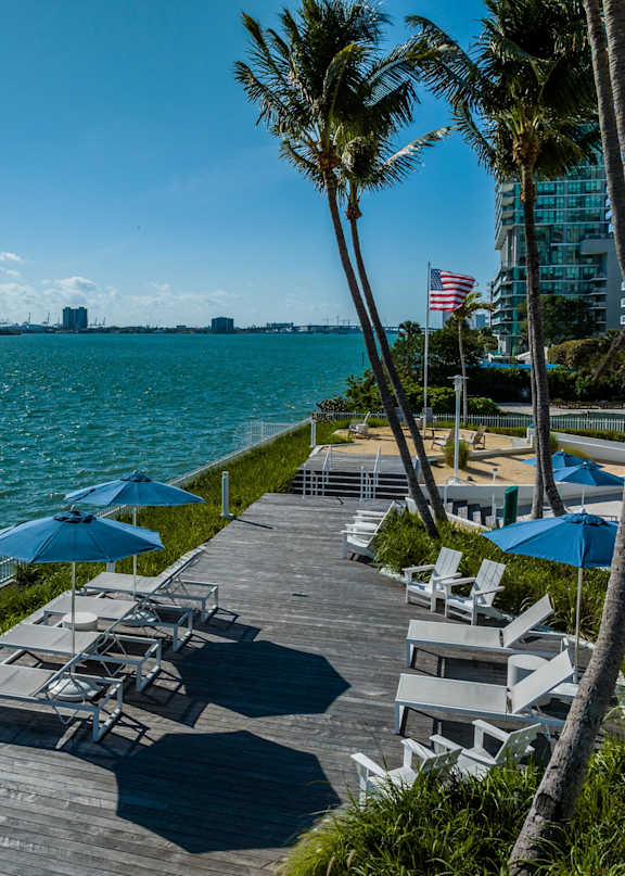 A wooden deck with white chairs and an umbrella overlooking a body of water. at The Hamilton, Miami, FL