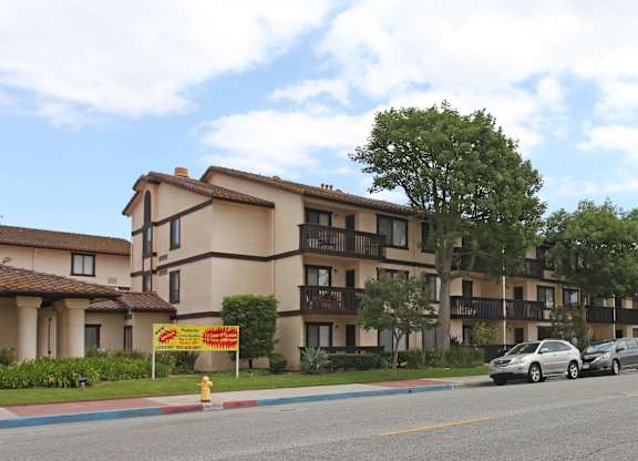 A row of apartment buildings with cars parked in front.