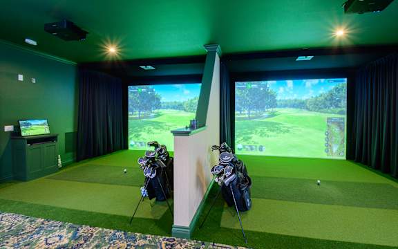 A golf simulator room with a screen and golf clubs.