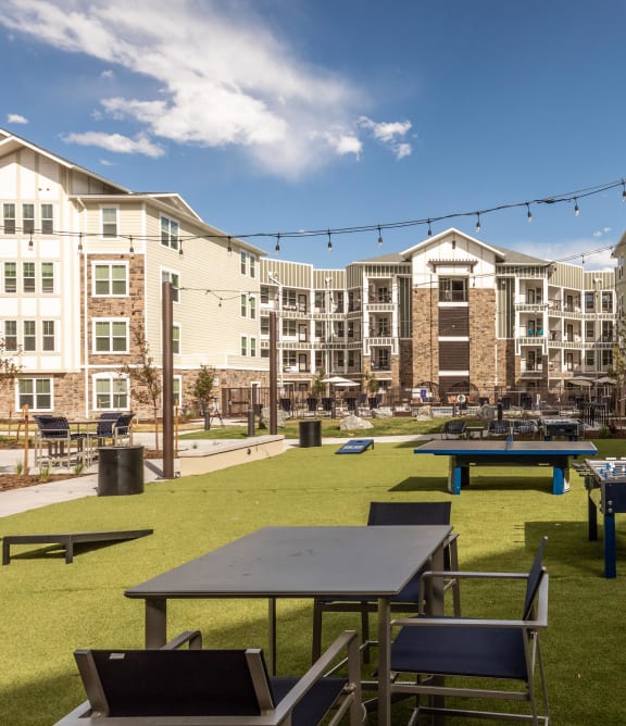 a grassy area with picnic tables and ping pong tables in front of an apartment building