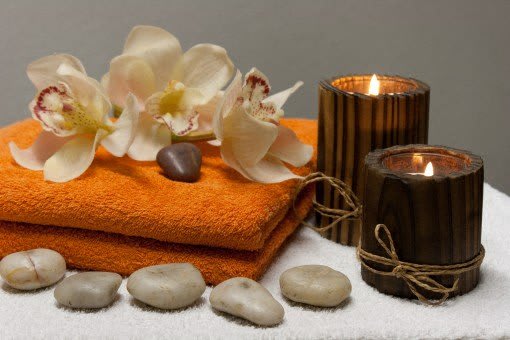 two candles and towels with rocks and orchid on a table