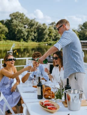 Friends drinking champagne and eating food beside a reflective lake