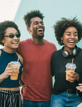 Three people are standing close together, each holding a cup with a straw, and appear to be enjoying a casual outing.