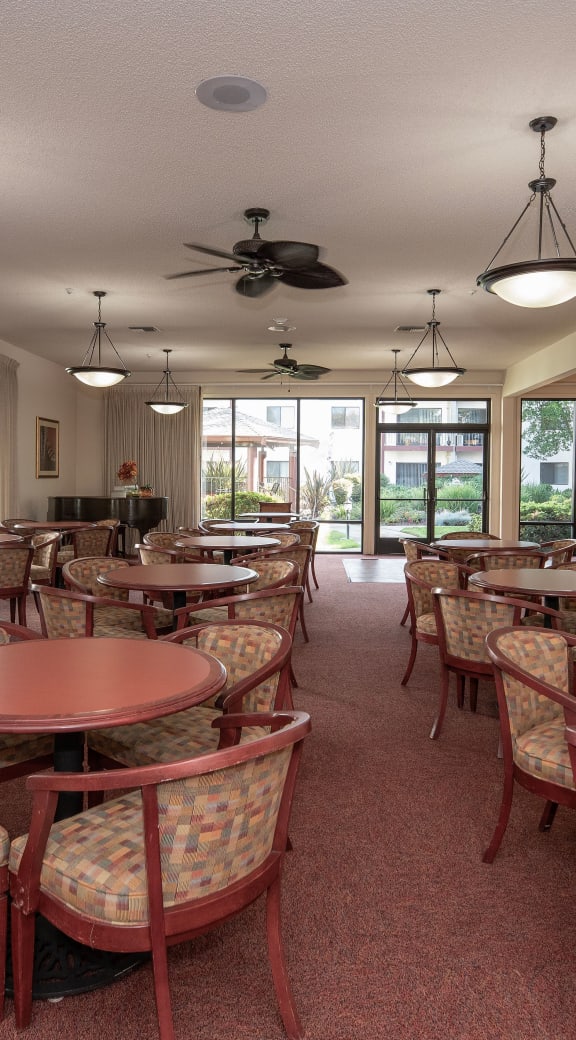 a large dining room with tables and chairs and windows at Roseville Commons Senior Living, Roseville, CA 95678