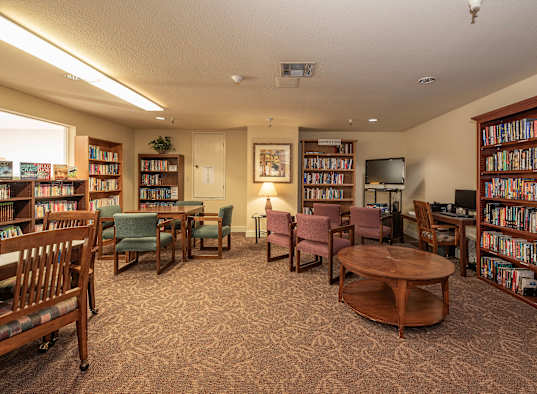 a library with tables and chairs and shelves of books at Hilltop Commons Senior Living, Grass Valley