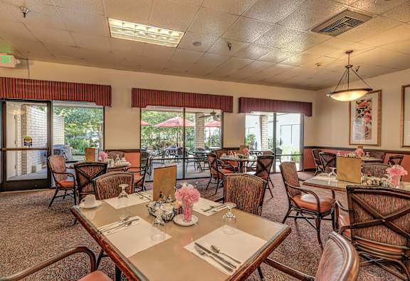 a dining room with tables and chairs and windows at Campus Commons Senior Living, California, 95825