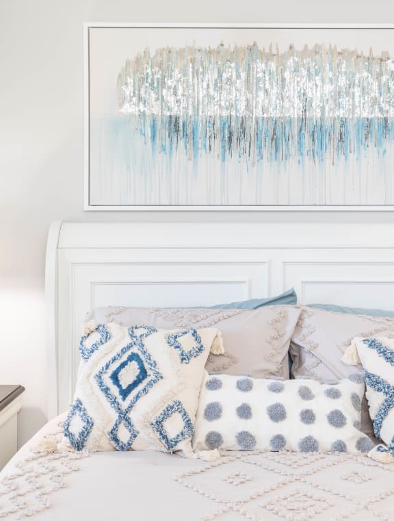 a bedroom with a white headboard and pillows and a blue and white artwork