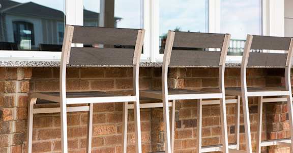 three wooden chairs on a porch with a brick wall