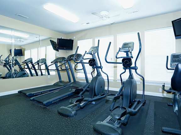 A gym with treadmills, elliptical machines, and a television.