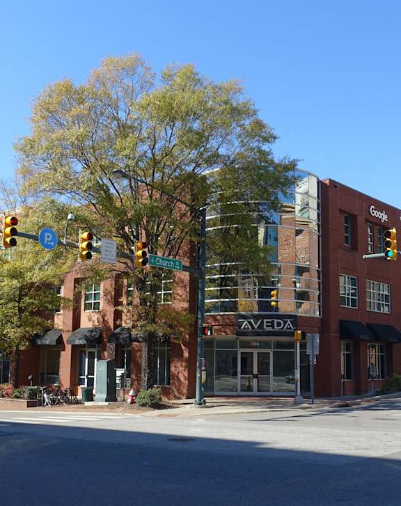 A street view of a city intersection with traffic lights and a building with a sign that says "AVEDA".