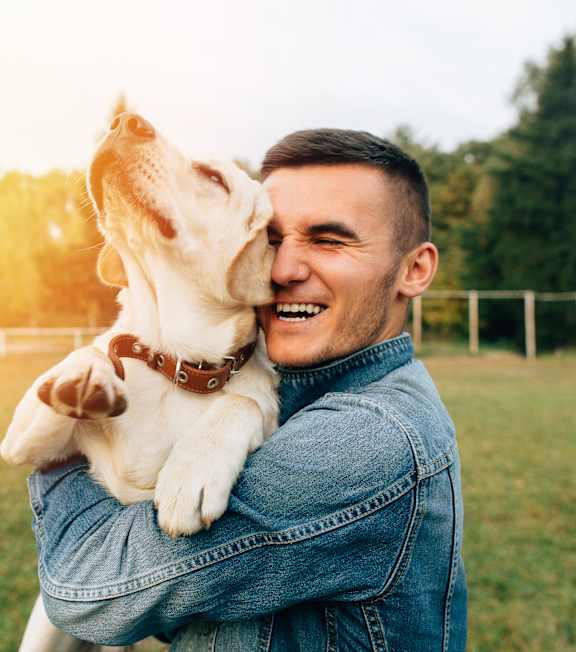 A man is hugging a white dog in a field.