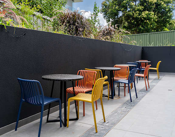 an outdoor seating area with tables and chairs against a black wall