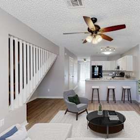 a living room with a ceiling fan and a kitchen with a bar